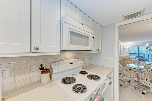 kitchen with white appliances, white cabinetry, a chandelier, and decorative backsplash