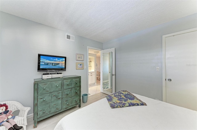 bedroom featuring connected bathroom, a textured ceiling, and light wood-type flooring