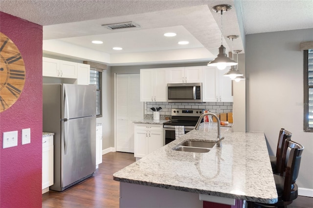 kitchen featuring light stone counters, white cabinets, hanging light fixtures, dark wood-type flooring, and appliances with stainless steel finishes