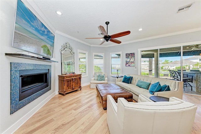 living room with light wood-type flooring, a tile fireplace, crown molding, and ceiling fan