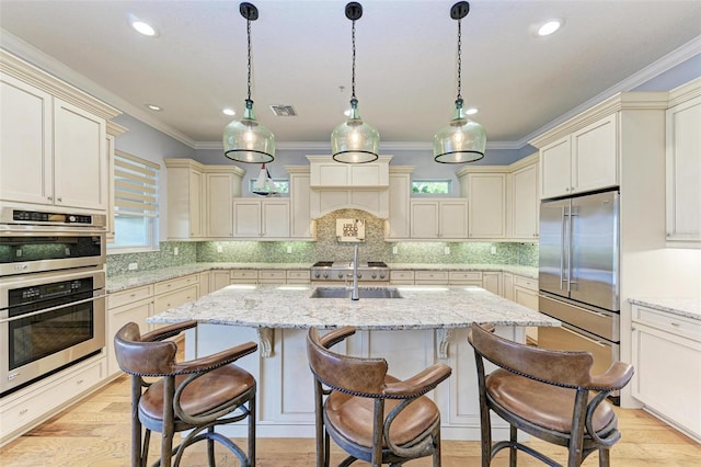 kitchen with an island with sink, stainless steel appliances, hanging light fixtures, and sink