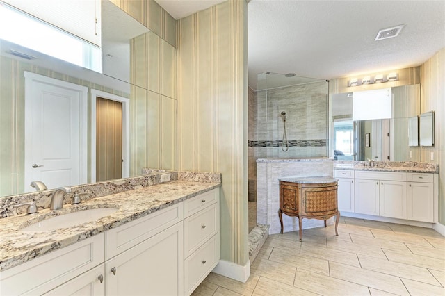 bathroom featuring a textured ceiling, vanity, and tiled shower