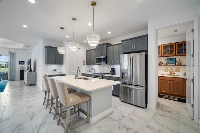 kitchen with an island with sink, appliances with stainless steel finishes, backsplash, sink, and decorative light fixtures