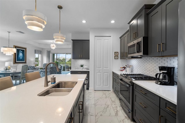 kitchen featuring sink, stainless steel appliances, pendant lighting, decorative backsplash, and an inviting chandelier