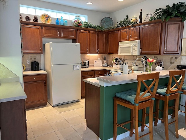 kitchen with light tile patterned flooring, kitchen peninsula, tasteful backsplash, white appliances, and a breakfast bar