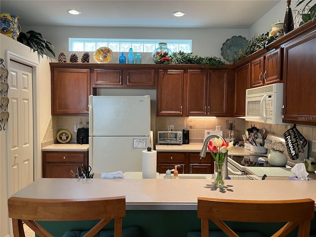 kitchen with a breakfast bar area, tasteful backsplash, and white appliances