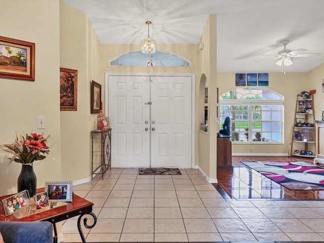 foyer entrance with a textured ceiling, light tile patterned floors, and ceiling fan with notable chandelier