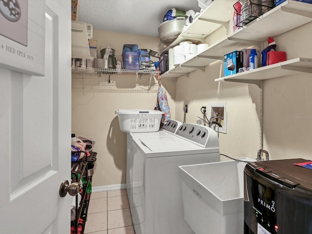 washroom featuring a textured ceiling, washing machine and dryer, light tile patterned floors, and sink