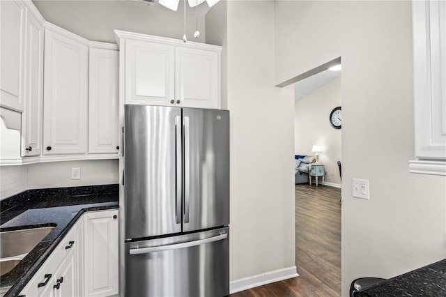 kitchen featuring ceiling fan, white cabinets, stainless steel fridge, dark hardwood / wood-style floors, and dark stone counters