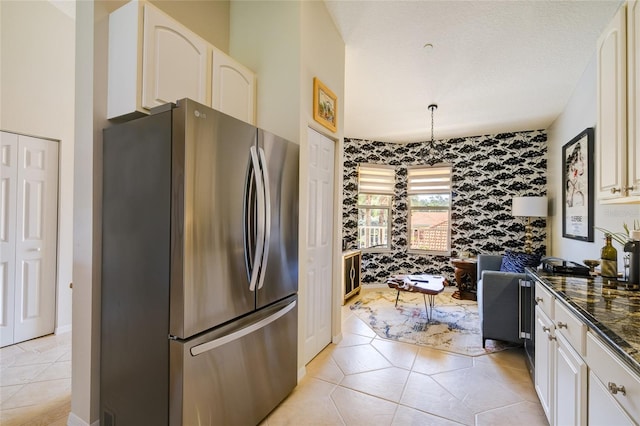 kitchen featuring dark stone countertops, white cabinets, stainless steel refrigerator, and light tile patterned floors