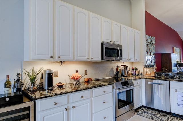 kitchen with appliances with stainless steel finishes, dark stone counters, vaulted ceiling, and white cabinets