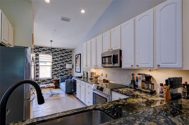 kitchen featuring appliances with stainless steel finishes, white cabinetry, vaulted ceiling, backsplash, and pendant lighting