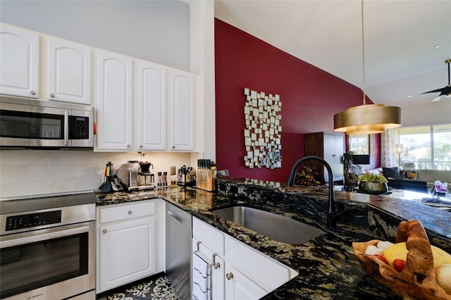 kitchen with hanging light fixtures, sink, white cabinetry, stainless steel appliances, and dark stone counters