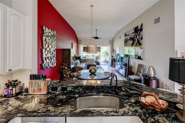 kitchen featuring dark stone countertops, white cabinets, lofted ceiling, ceiling fan, and sink