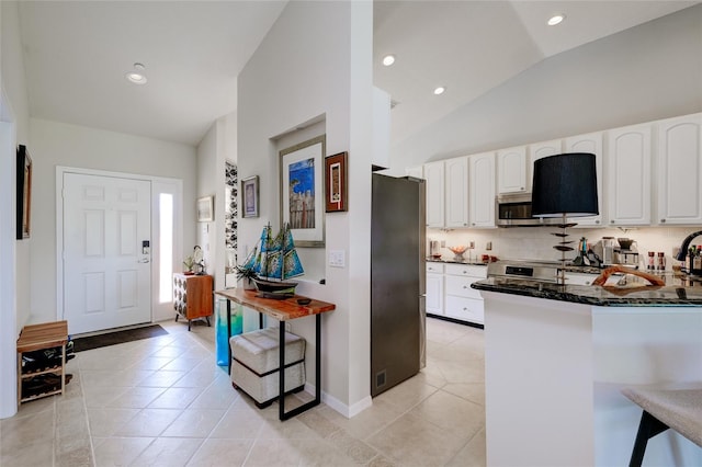 kitchen featuring white cabinets, a breakfast bar area, stainless steel appliances, lofted ceiling, and dark stone counters