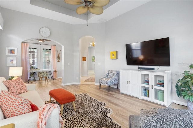 living room featuring light wood-type flooring, a tray ceiling, a towering ceiling, and ceiling fan