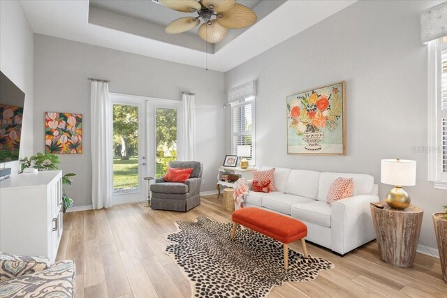 living room with a raised ceiling, light hardwood / wood-style floors, and ceiling fan