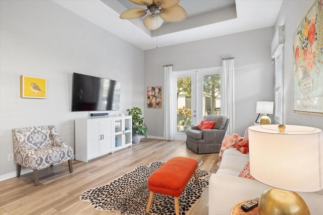 living room with a raised ceiling, light hardwood / wood-style floors, and ceiling fan