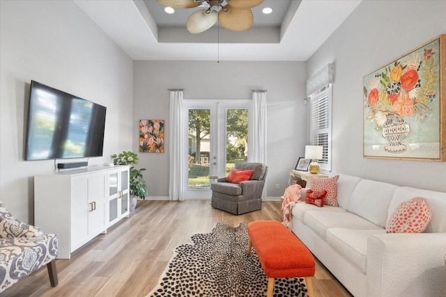 living room with ceiling fan, light wood-type flooring, and a raised ceiling