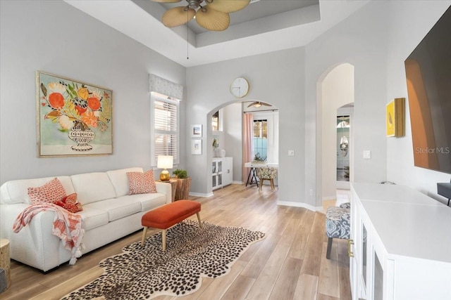 living room with light hardwood / wood-style flooring, a tray ceiling, and ceiling fan