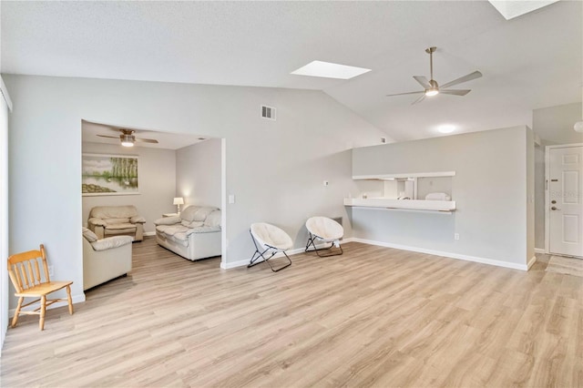 living room featuring lofted ceiling with skylight, light wood-type flooring, and ceiling fan