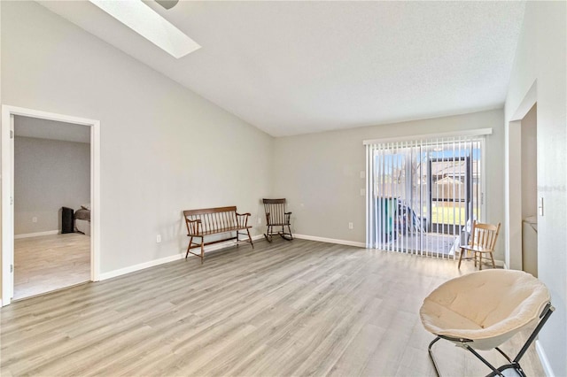 sitting room featuring vaulted ceiling with skylight and light wood-type flooring