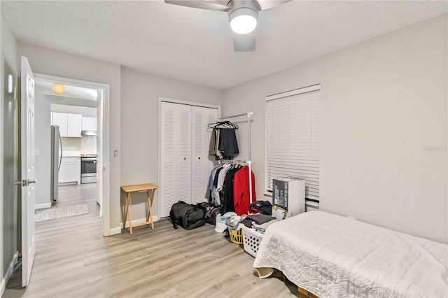 bedroom featuring stainless steel fridge, ceiling fan, a textured ceiling, light hardwood / wood-style floors, and a closet