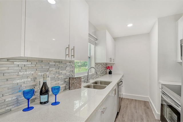 kitchen with light stone counters, sink, white cabinetry, stainless steel appliances, and light wood-type flooring