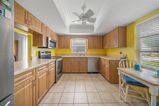 kitchen with crown molding, a tray ceiling, sink, stainless steel appliances, and light tile patterned floors