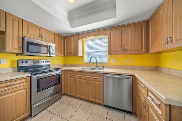 kitchen with light tile patterned flooring, ornamental molding, sink, stainless steel appliances, and a tray ceiling