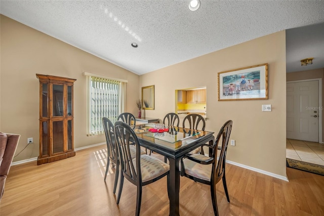 dining space featuring a textured ceiling, light wood-type flooring, and lofted ceiling