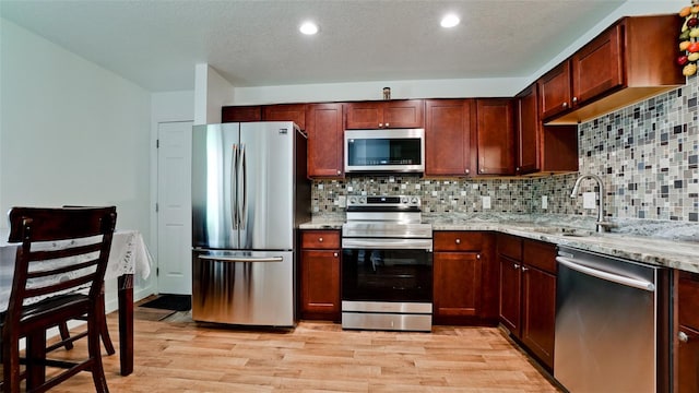 kitchen featuring light wood-type flooring, sink, decorative backsplash, stainless steel appliances, and light stone countertops