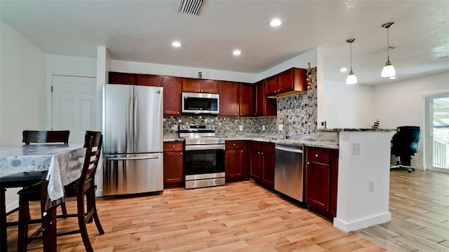 kitchen with hanging light fixtures, kitchen peninsula, light hardwood / wood-style flooring, stainless steel appliances, and light stone countertops