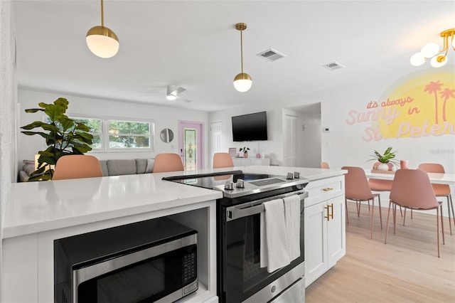 kitchen featuring appliances with stainless steel finishes, white cabinets, ceiling fan with notable chandelier, pendant lighting, and light wood-type flooring