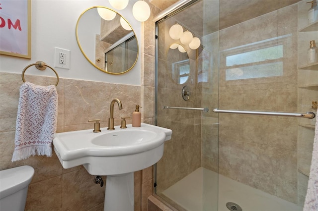 bathroom featuring tile walls, sink, a shower with shower door, and toilet