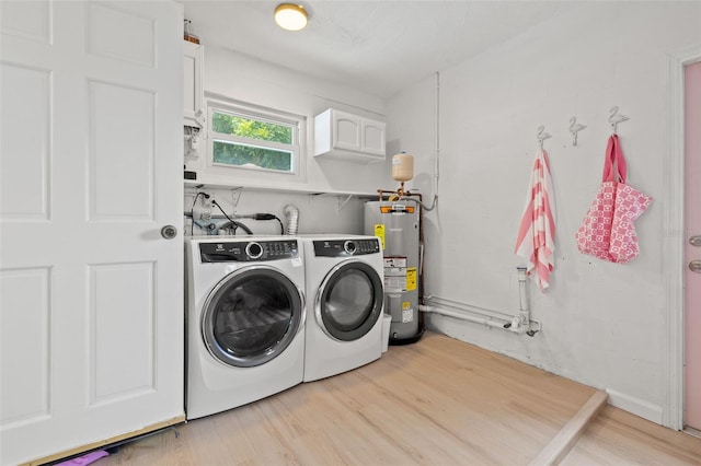 clothes washing area featuring light hardwood / wood-style floors, water heater, washing machine and dryer, and cabinets