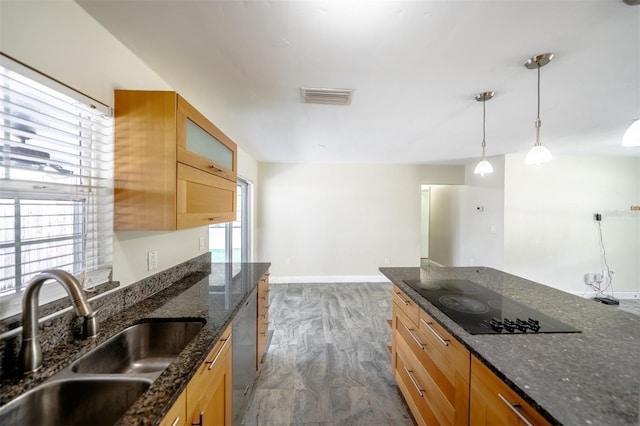 kitchen with black electric cooktop, dark stone countertops, dark wood-type flooring, decorative light fixtures, and sink