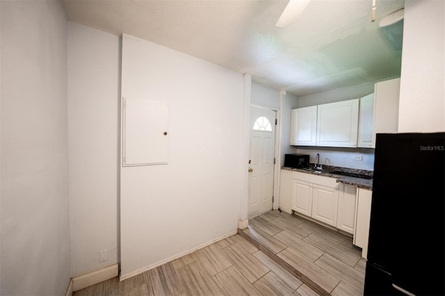 kitchen with light hardwood / wood-style flooring, white cabinets, dark stone countertops, and black refrigerator