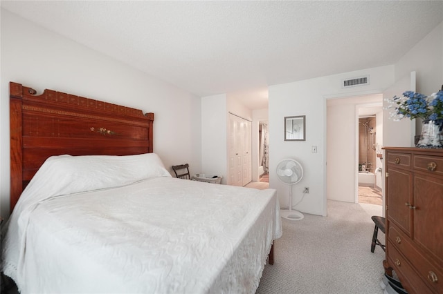 bedroom with light carpet, a textured ceiling, a closet, and ensuite bath