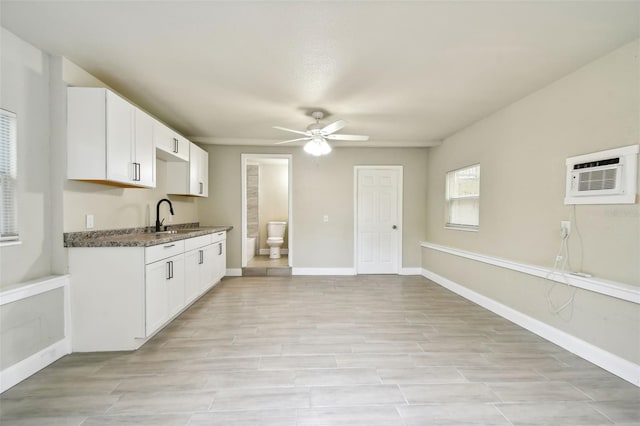 3419 19th St E, Bradenton, FL 34208 - kitchen with dark countertops, a ceiling fan, a wall unit AC, a sink, and white cabinetry