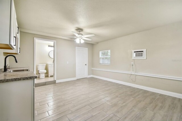 interior space with light wood-type flooring, a textured ceiling, sink, a wall mounted air conditioner, and ceiling fan