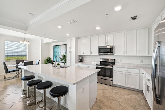 kitchen with hanging light fixtures, an island with sink, appliances with stainless steel finishes, a notable chandelier, and white cabinetry