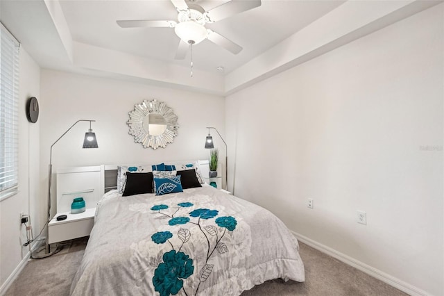 carpeted bedroom with a raised ceiling and ceiling fan