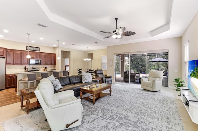 living room featuring ceiling fan with notable chandelier, light hardwood / wood-style floors, and a tray ceiling