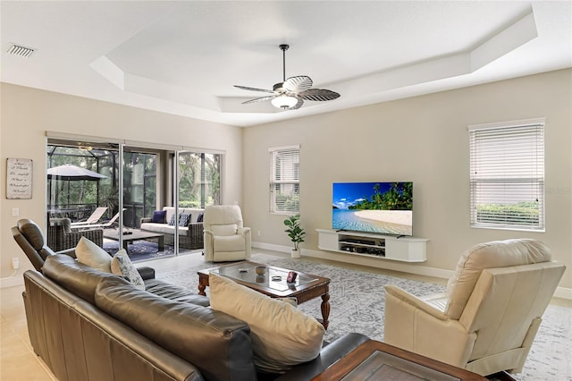 tiled living room with ceiling fan and a raised ceiling