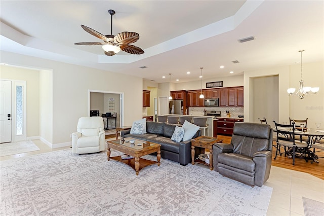 living room with ceiling fan with notable chandelier, a tray ceiling, and light tile patterned floors