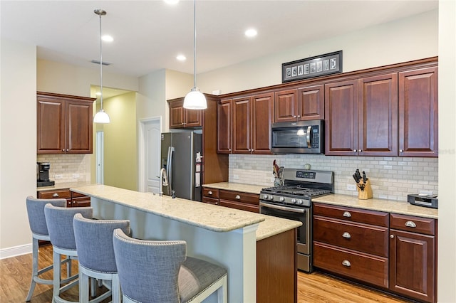 kitchen with pendant lighting, a kitchen island with sink, appliances with stainless steel finishes, and a kitchen bar