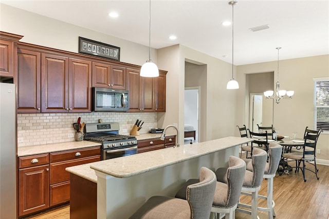 kitchen featuring hanging light fixtures, a breakfast bar, stainless steel appliances, light hardwood / wood-style flooring, and a chandelier