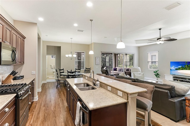 kitchen with appliances with stainless steel finishes, ceiling fan with notable chandelier, pendant lighting, light hardwood / wood-style flooring, and sink