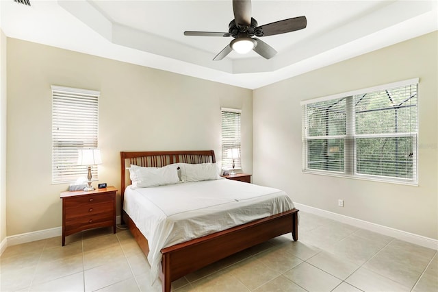 bedroom featuring a raised ceiling, light tile patterned floors, and ceiling fan